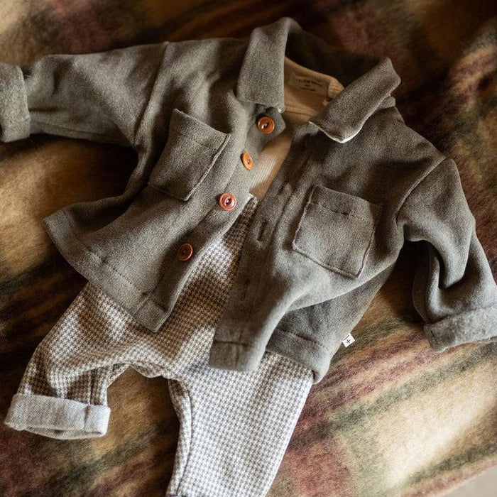 A baby clothing set laid flat on a soft plaid blanket, featuring a muted gray wool button-front cardigan with orange buttons over a cream shirt, paired with light gray and white gingham pants.