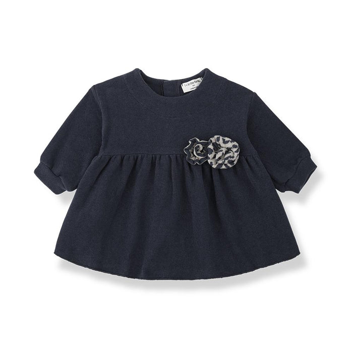 A navy blue short-sleeve baby dress with a gathered peplum waist and a gray and white patterned fabric flower applique on the chest, shown on a white background.