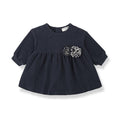 A navy blue short-sleeve baby dress with a gathered peplum waist and a gray and white patterned fabric flower applique on the chest, shown on a white background.