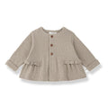 A light taupe knit cardigan for toddlers, featuring three brown buttons down the front, ruffled trim at the waist and cuffs, and a crew neck, shown on a white background.