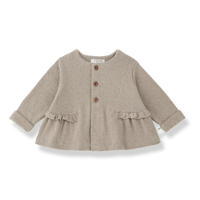 A light taupe knit cardigan for toddlers, featuring three brown buttons down the front, ruffled trim at the waist and cuffs, and a crew neck, shown on a white background.