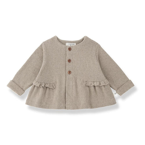 A light taupe knit cardigan for toddlers, featuring three brown buttons down the front, ruffled trim at the waist and cuffs, and a crew neck, shown on a white background.