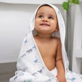 Baby wrapped in a hooded towel with animal patterns, sitting on a white surface.