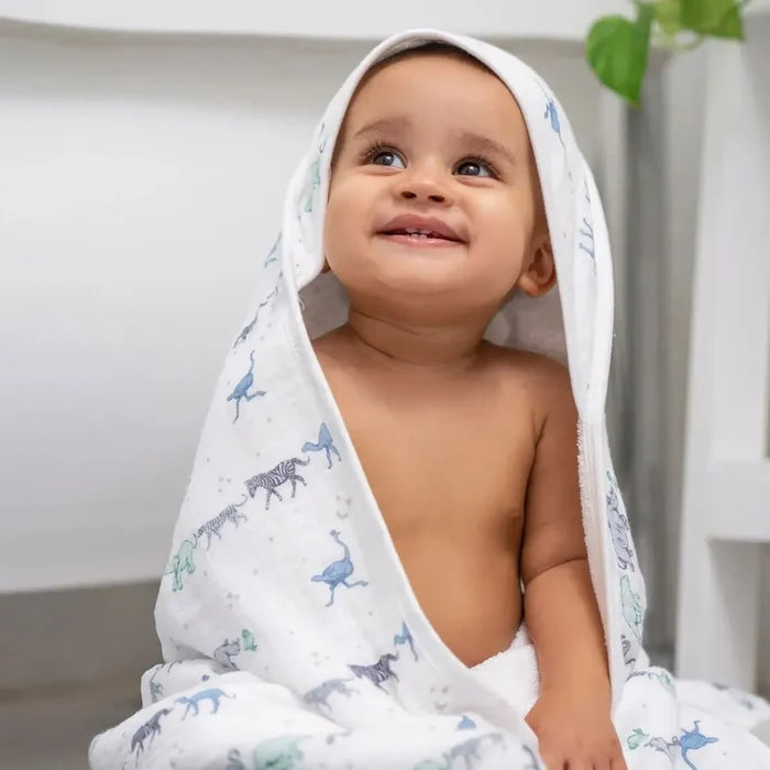 Baby wrapped in a hooded towel with animal patterns, sitting on a white surface.
