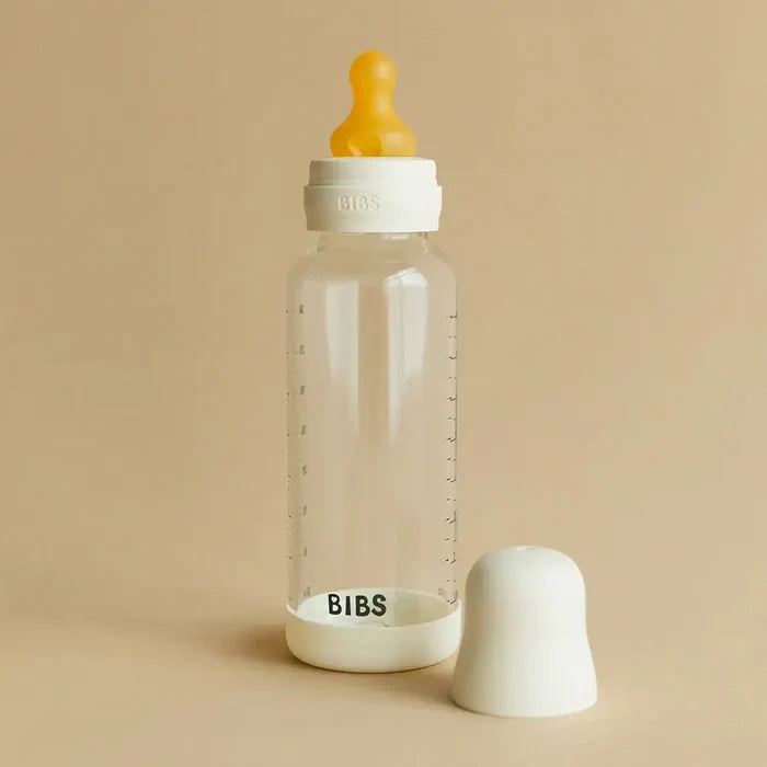 Clear baby bottle with orange nipple and white cap on a beige background