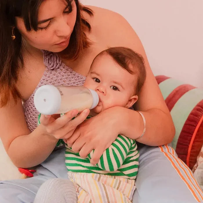 Woman holding a baby and feeding them with a bottle against a neutral background