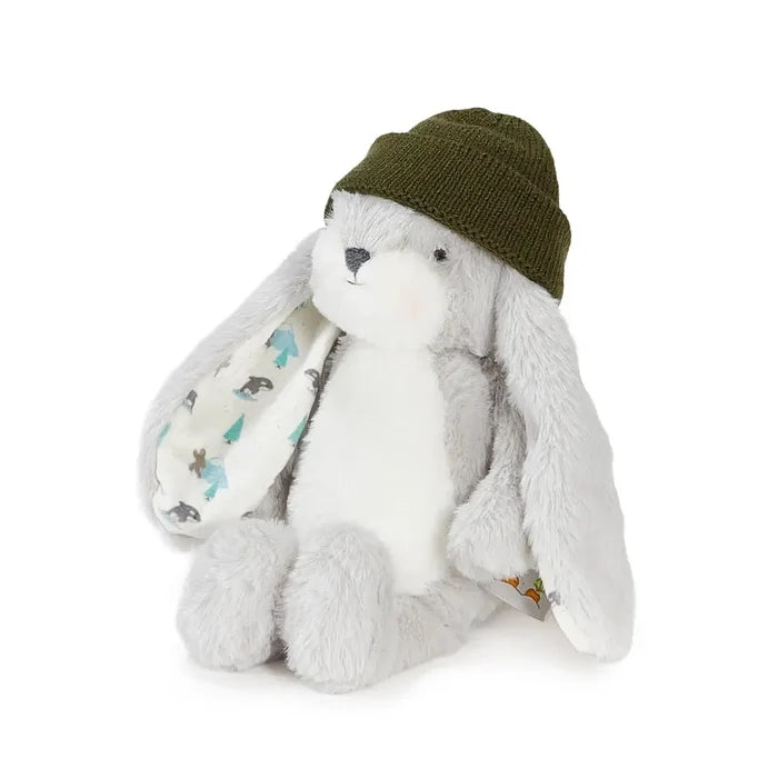 A plush stuffed bunny toy in light gray and white, wearing an olive green knit beanie and holding a patterned white blanket, photographed on a clean white background.