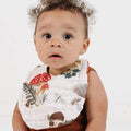 Baby wearing a floral bib and brown outfit on a white background