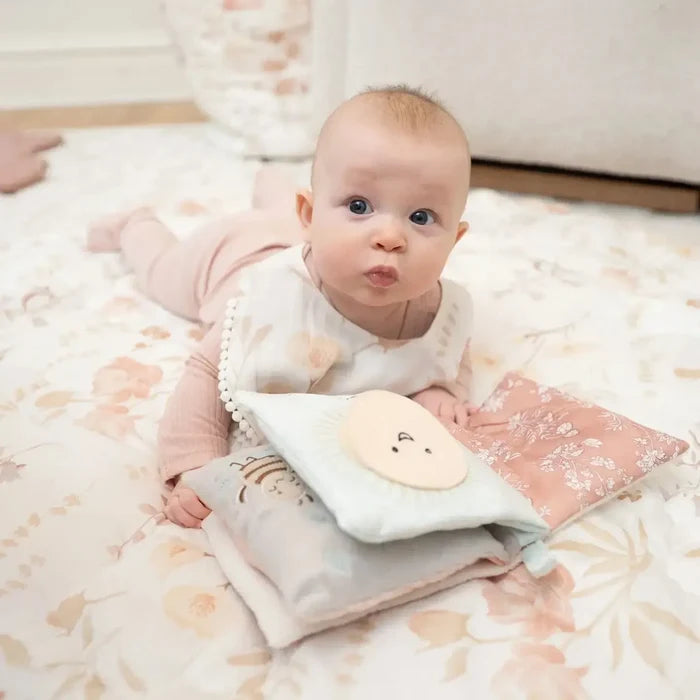 Baby lying on a floral blanket with soft toys