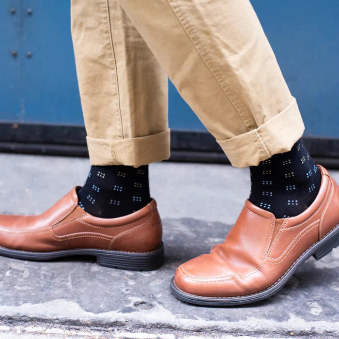 Brown shoes and beige pants with black patterned socks on a concrete floor.