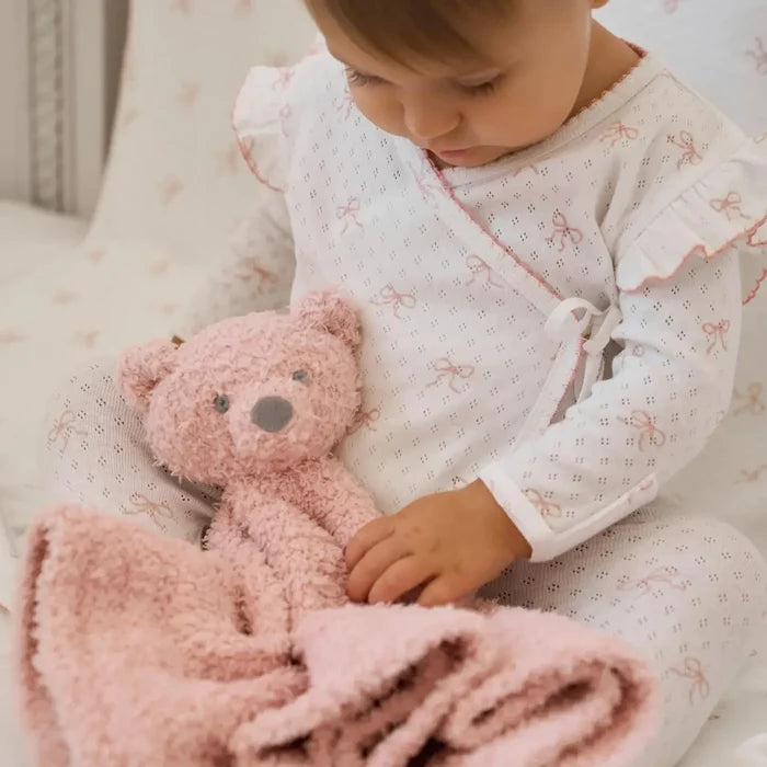 Child holding a pink teddy bear and blanket on a soft surface