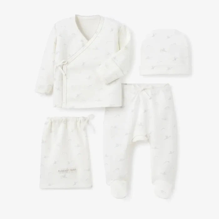 A baby clothing set laid out on a light gray background, including a long-sleeve wrap-style top, footed pants, a drawstring bag, and a beanie. The items are off-white with a very subtle, faint pastel rainbow pattern.