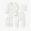 A baby clothing set laid out on a light gray background, including a long-sleeve wrap-style top, footed pants, a drawstring bag, and a beanie. The items are off-white with a very subtle, faint pastel rainbow pattern.