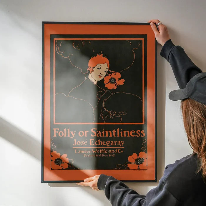 Folly or Saintliness vintage poster of a woman by Ethel Reed being hung on a wall in a black frame