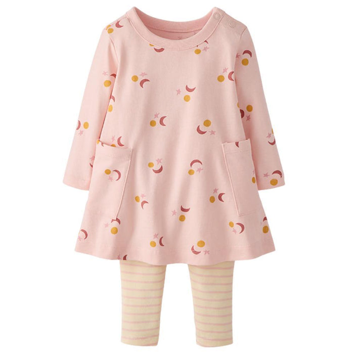A toddler girl's two-piece set featuring a light pink long-sleeve tunic dress with a celestial print of crescent moons, stars, and dots, paired with light pink and white striped leggings.