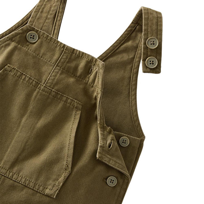 Close-up detail of olive green canvas bib overalls showing the shoulder straps with snap buttons and the front bib pocket.