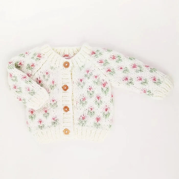A cream-colored knit baby cardigan sweater with a delicate pink and green floral pattern, featuring three wooden buttons on the front, laid flat on a white background.