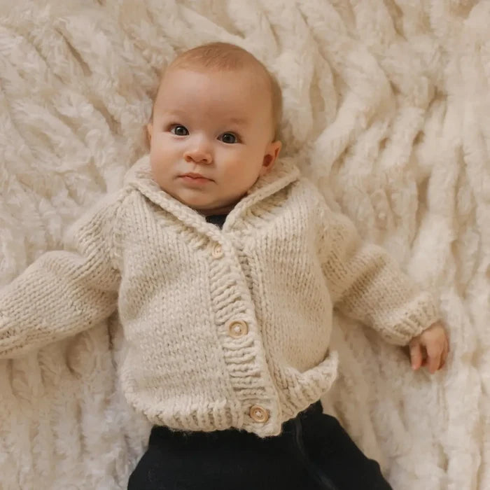 Baby wearing a beige knitted cardigan on a textured beige blanket