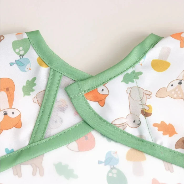 Close-up of a baby garment with a white base, light green trim, and a colorful woodland animal print including foxes, rabbits, birds, and leaves.