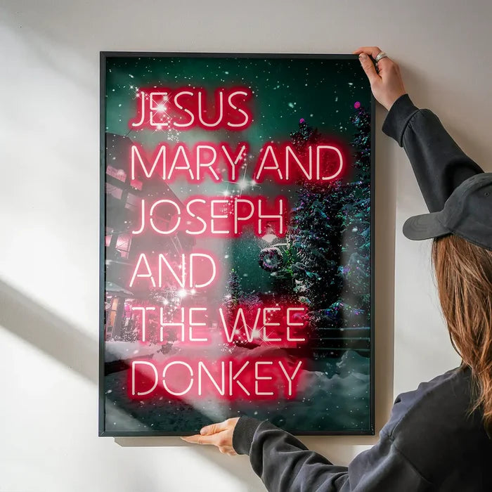 Jesus, Mary, Joseph & The Wee Donkey Christmas Print being hung on a wall in a black frame