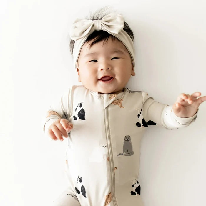 Baby wearing a onesie with animal prints and a headband, standing against a white background