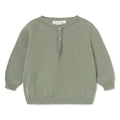 A sage green knit baby sweater with three wooden buttons on the chest, laid flat against a white background.