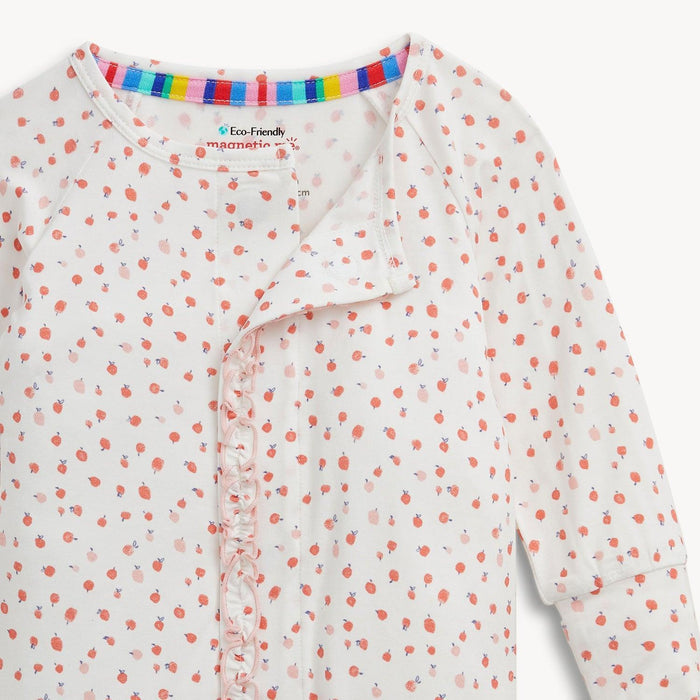 A close-up of a baby long-sleeve romper with a white base, covered in a small pink apple pattern, and a ruffled front placket depicting the magnetic closure