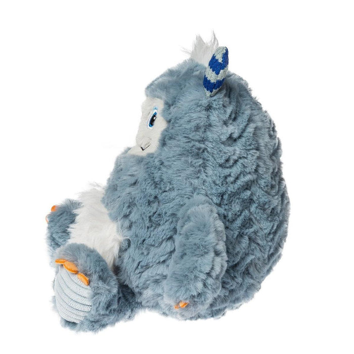 A plush monster toy in a sitting position, featuring shaggy light blue-gray fur, a white snout and belly, a blue and white horn, and small orange accents on its feet.