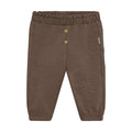 A pair of toddler jogger pants in a heathered brown fabric, featuring a gold heart-shaped button closure at the waist and a small white brand tag on the side, set against a solid black background.