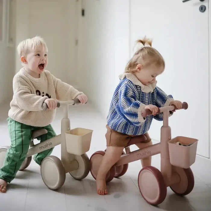 Two children playing with balance bikes indoors.