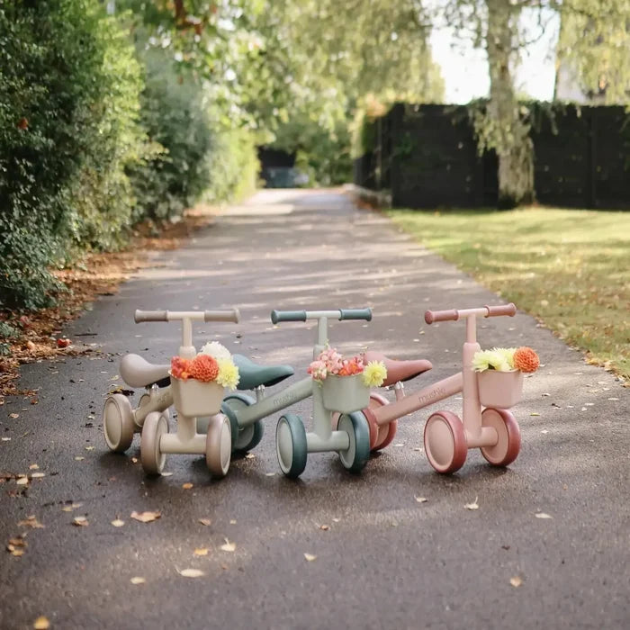 Three children's tricycles on a paved path with greenery in the background