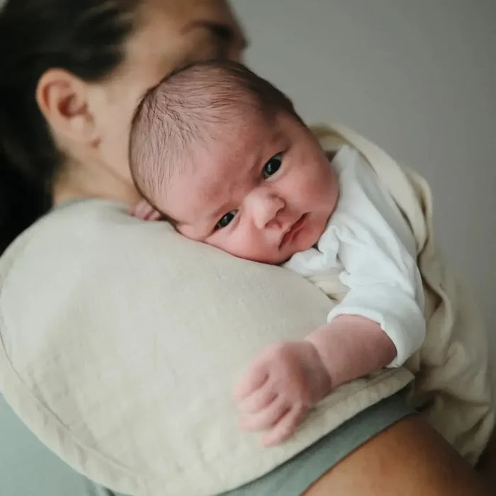 Newborn baby being held by a person wearing a white shirt and beige pants.