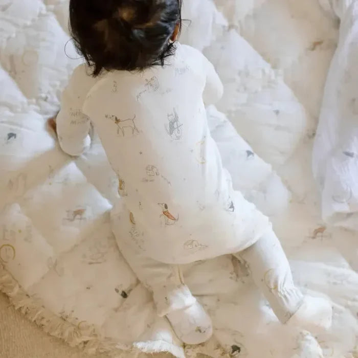 Baby in a white outfit sitting on a textured white blanket
