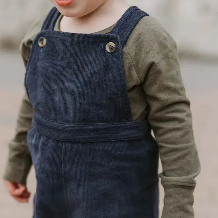Child wearing navy blue corduroy overalls with a green long-sleeve shirt.
