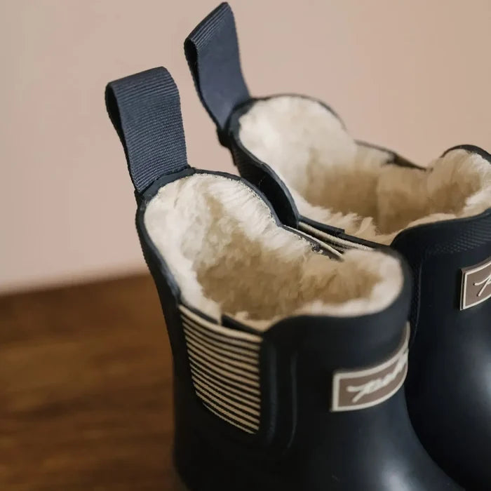 Pair of black boots with white fur lining on a wooden floor.