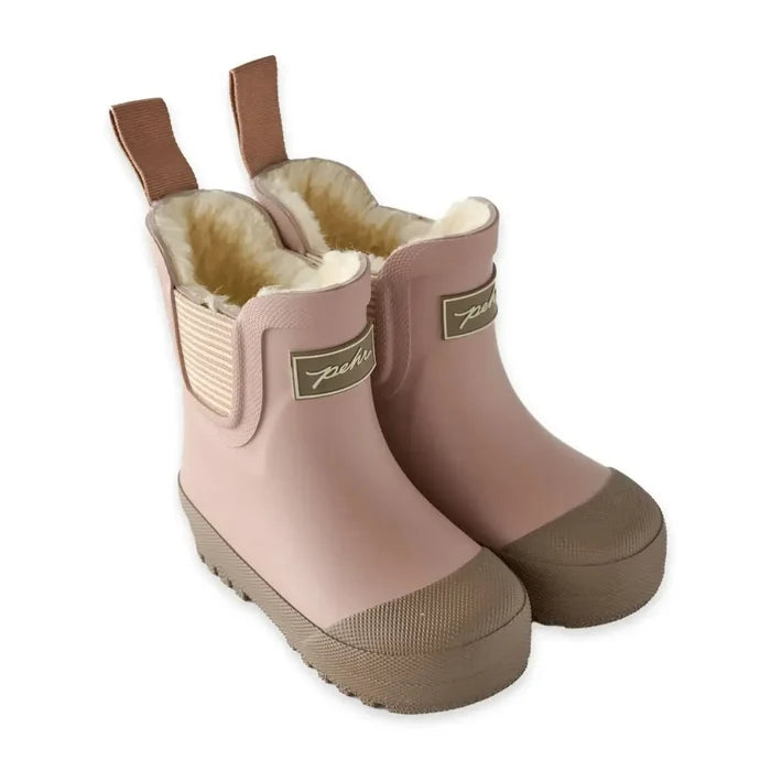 A pair of children's rain boots in dusty pink with tan rubber toe caps and pull tabs, featuring a soft cream fleece lining and a small metallic brand plaque on the side.