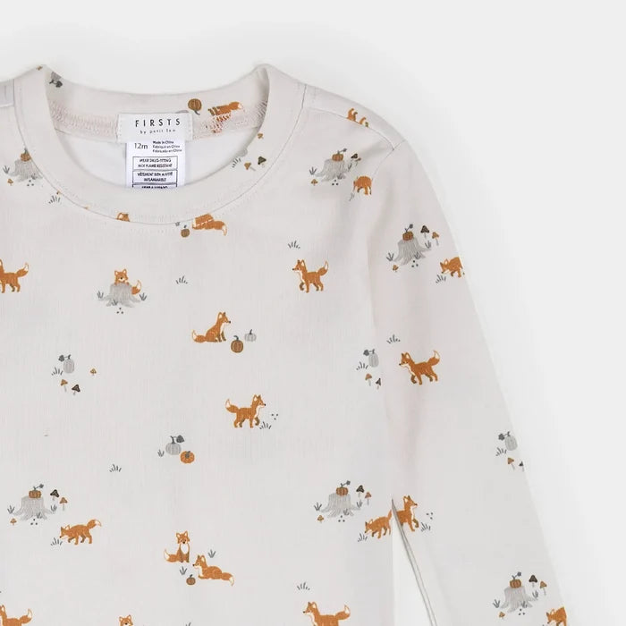 A close-up of a long-sleeve children's top in off-white, featuring a playful all-over print of orange foxes, gray rabbits, and small brown acorns. The brand name 'FIRSTS' is visible on the inner neck label.