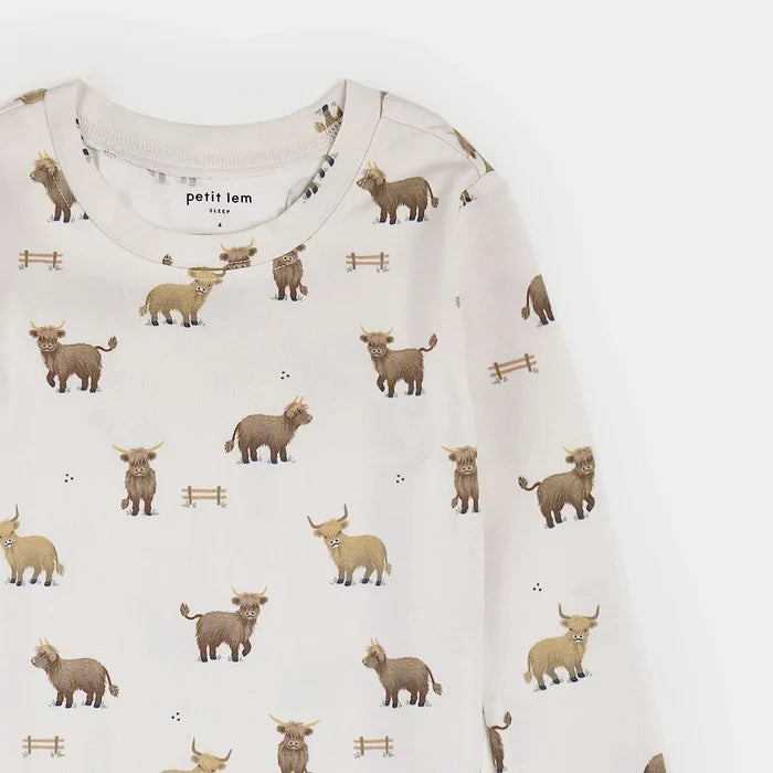 A close-up of a long-sleeve baby top by Petit Lem, featuring a white base with an all-over print of brown and beige Highland cows and small wooden fence motifs.