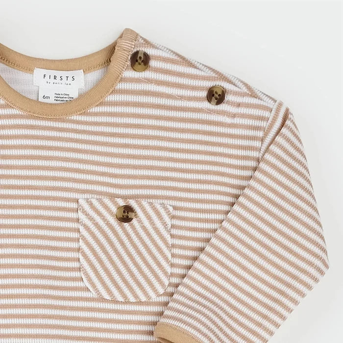A close-up of a baby long-sleeve top by FIRSTS, featuring thin beige and white horizontal stripes, a chest pocket with a decorative brown button, and matching brown buttons on the shoulders.