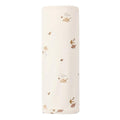 A rolled-up baby swaddle blanket in a warm cream color, printed with a delicate pattern of small brown and gold woodland animals and leaves.