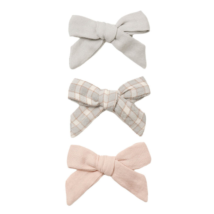 Three fabric bow hair clips in soft neutral tones, including a solid light gray bow, a beige and gray plaid bow, and a solid pale pink bow, arranged vertically on a white background.