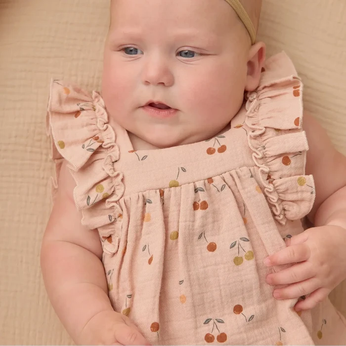 Baby wearing a pink dress with ruffles and a bow headband, sitting on a textured surface.