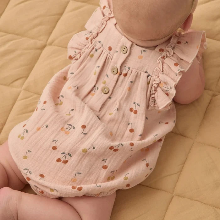 Baby wearing a pink floral dress on a beige quilted surface