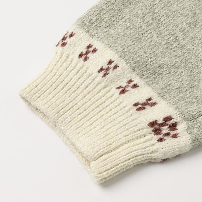 Close-up of a knit sweater cuff in a heathered sage green color, featuring a cream ribbed hem with a brown Fair Isle pattern.