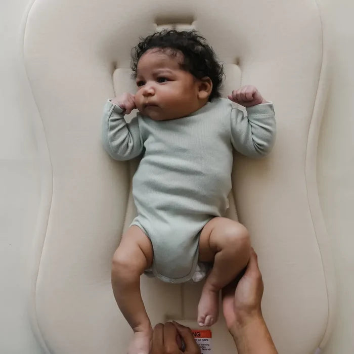 Infant laying on a cream colored baby lounger.