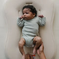Infant laying on a cream colored baby lounger.
