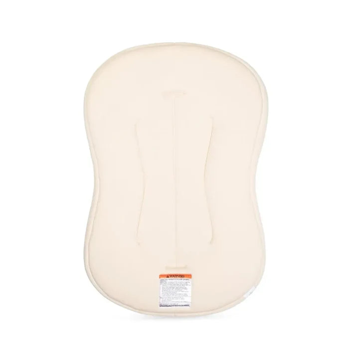 A cream-colored baby support cushion or diaper pad shown from the back, featuring molded ergonomic support channels and a small orange and white label near the bottom center, set against a plain white background.