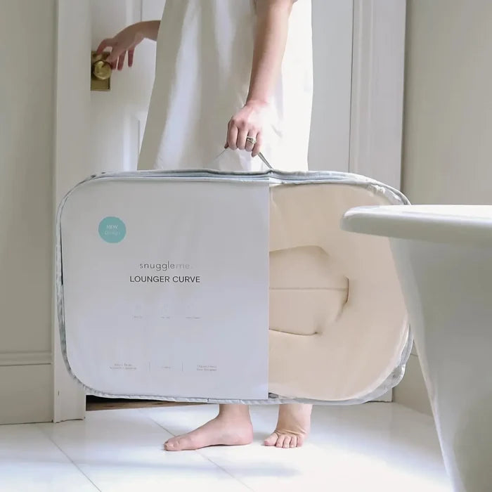 Woman in bathroom holding cream colored baby lounger in manufacturing packaging.