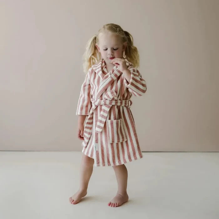 Young girl wearing a blush and white striped robe against a plain background
