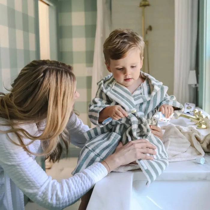 Woman helping a child put on a striped robe in a bathroom.